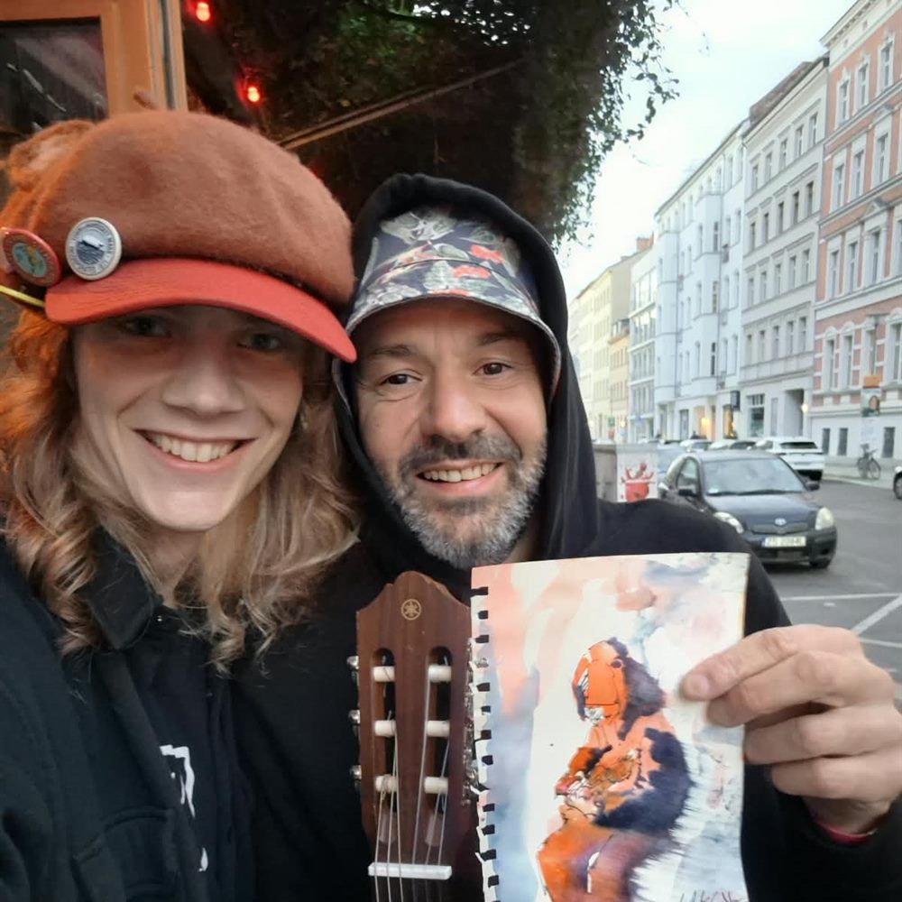 Aydan and a musician laughing and showing his watercolour portrait, drawn outside the Schokoladen in Berlin