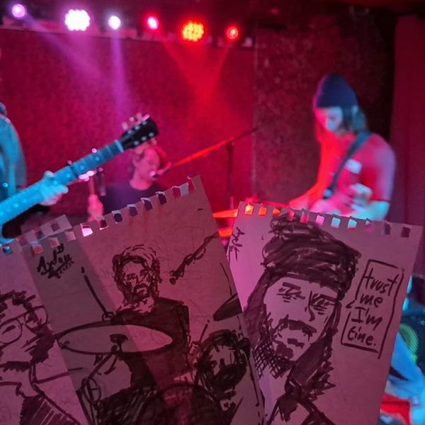 A band live on stage, drawings held up in front